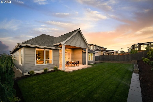 back house at dusk featuring a patio area and a lawn