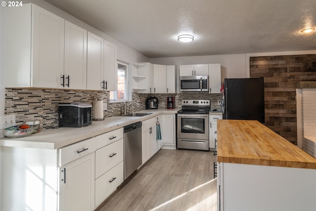 kitchen featuring light hardwood / wood-style flooring, butcher block countertops, decorative backsplash, white cabinets, and appliances with stainless steel finishes