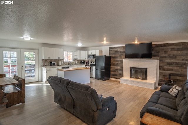 living room featuring wood walls, light hardwood / wood-style flooring, french doors, and a brick fireplace