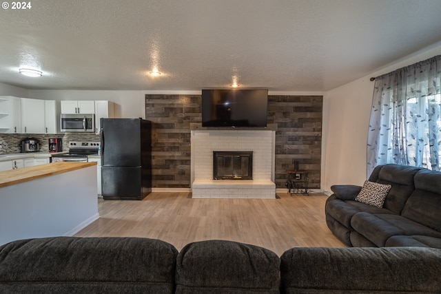 living room with a brick fireplace, a textured ceiling, wooden walls, and light hardwood / wood-style flooring