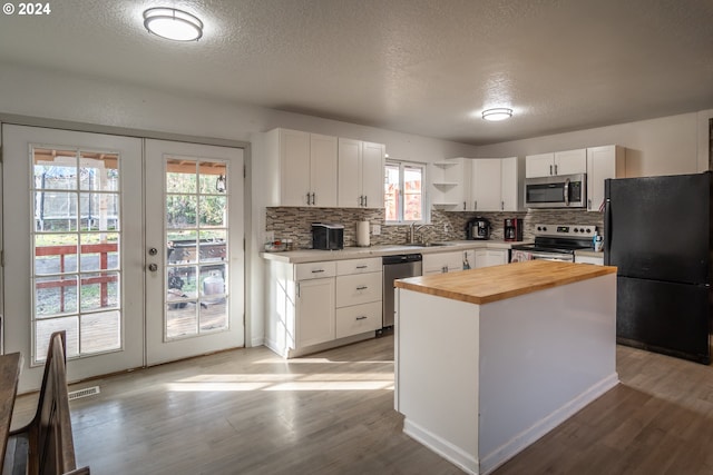 kitchen featuring appliances with stainless steel finishes, light wood-type flooring, french doors, white cabinetry, and butcher block counters