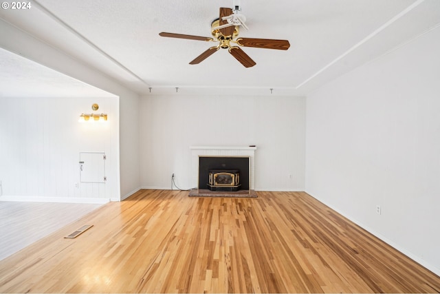 unfurnished living room with light hardwood / wood-style floors, ceiling fan, a textured ceiling, and a wood stove