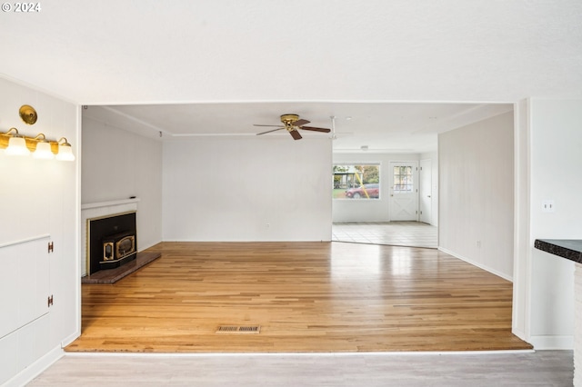 unfurnished living room with ceiling fan, hardwood / wood-style floors, and a wood stove