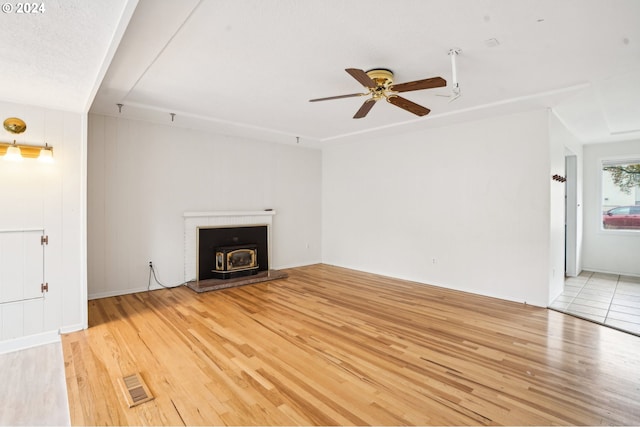 unfurnished living room with ceiling fan, a wood stove, light hardwood / wood-style floors, and a textured ceiling