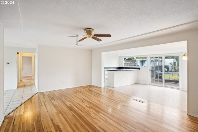 unfurnished living room with ceiling fan, a textured ceiling, and light hardwood / wood-style floors