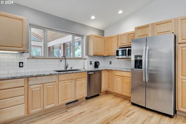 kitchen with light brown cabinetry, stainless steel appliances, lofted ceiling, and a sink