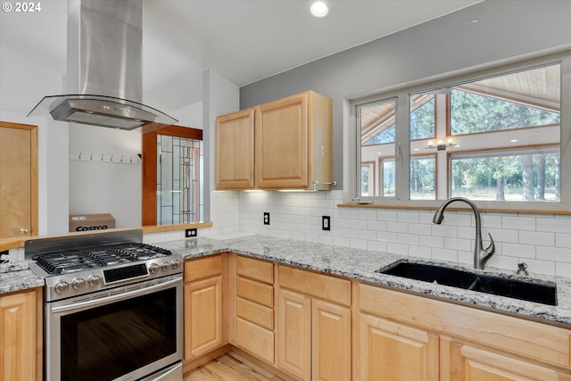 kitchen with light brown cabinets, a sink, light stone counters, island range hood, and stainless steel range with gas stovetop