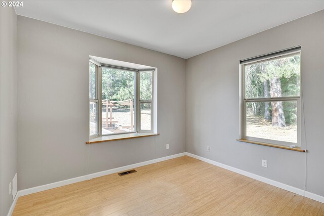 spare room featuring wood finished floors, visible vents, and baseboards