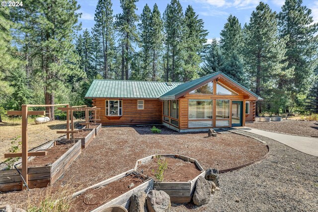 rear view of property with a garden, log exterior, and metal roof