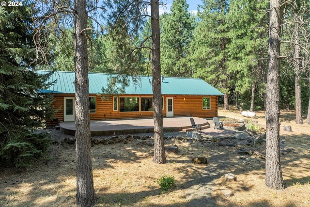 back of house featuring log siding, metal roof, a view of trees, and a patio area