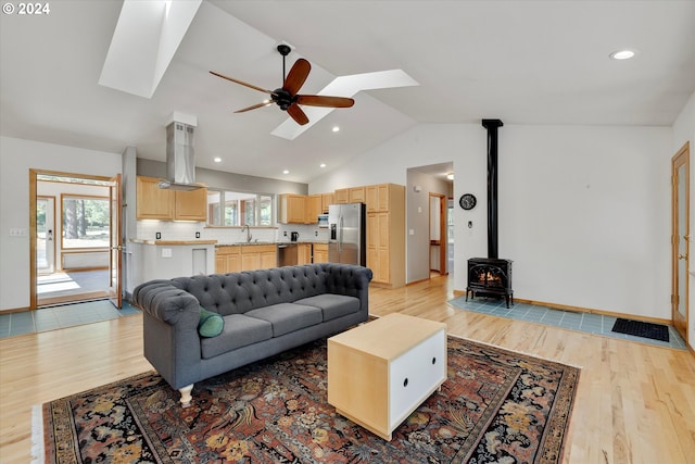 living room featuring light wood finished floors, a wood stove, recessed lighting, ceiling fan, and lofted ceiling with skylight