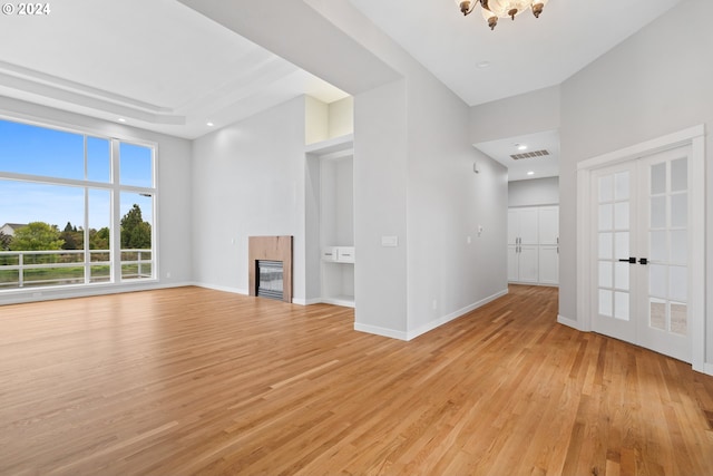 unfurnished living room with french doors, an inviting chandelier, and light hardwood / wood-style flooring