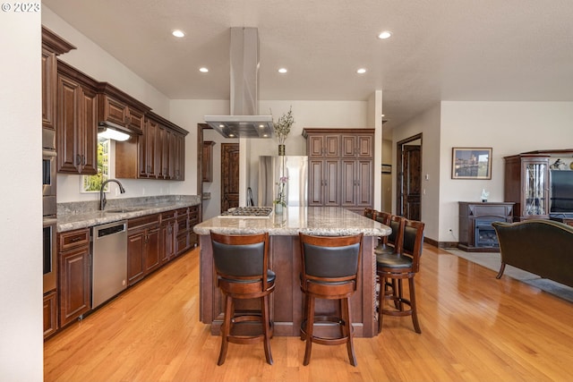 kitchen featuring stainless steel appliances, an island with sink, sink, island range hood, and light wood-type flooring