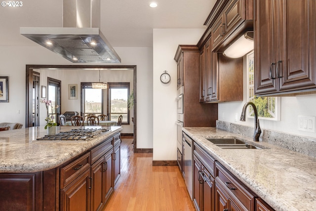 kitchen with sink, light wood-type flooring, light stone counters, island range hood, and stainless steel appliances