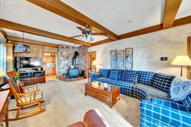 living room featuring carpet floors, beam ceiling, ceiling fan, and a wood stove