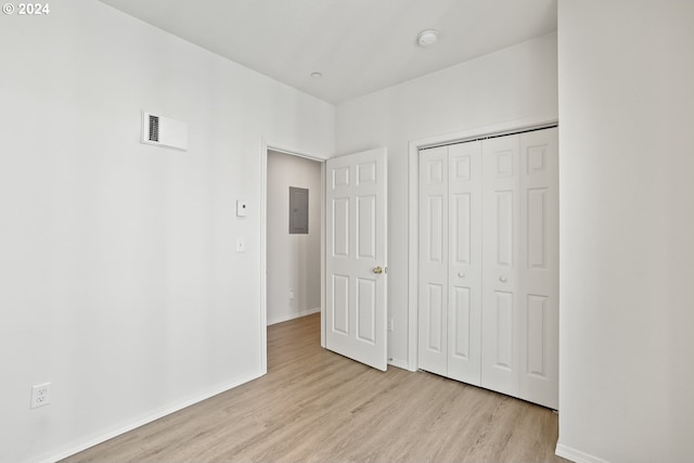 unfurnished bedroom featuring electric panel, light hardwood / wood-style floors, and a closet