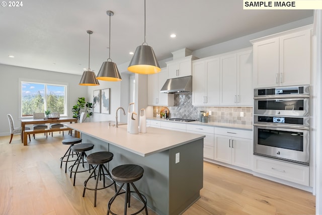 kitchen featuring appliances with stainless steel finishes, white cabinets, decorative light fixtures, and a kitchen island with sink