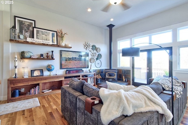 living room with a wood stove, ceiling fan, light hardwood / wood-style floors, and plenty of natural light