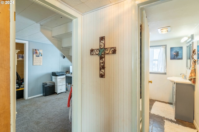 corridor featuring dark carpet, wooden walls, and sink