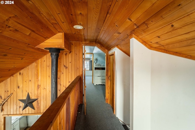 hallway with wood walls, dark carpet, lofted ceiling, and wooden ceiling