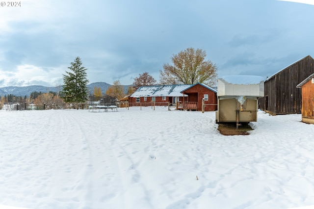 yard layered in snow featuring a mountain view, an outbuilding, and a trampoline