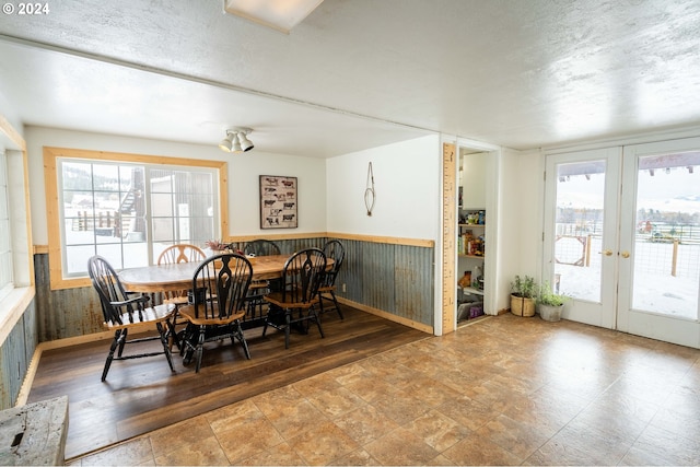 dining area featuring wooden walls, french doors, a healthy amount of sunlight, and a textured ceiling