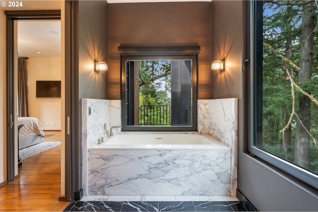 bathroom with tiled tub and wood-type flooring