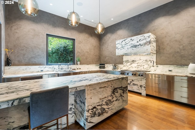 kitchen featuring light hardwood / wood-style floors, backsplash, stainless steel gas cooktop, exhaust hood, and decorative light fixtures