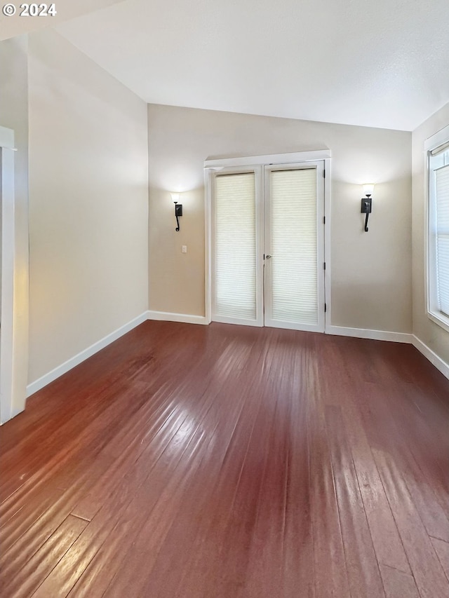 empty room with vaulted ceiling and hardwood / wood-style flooring