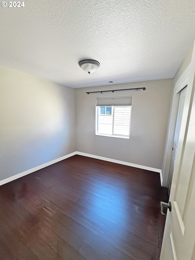 empty room with a textured ceiling and dark hardwood / wood-style flooring