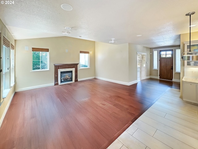 unfurnished living room featuring a textured ceiling, vaulted ceiling, ceiling fan, and light hardwood / wood-style flooring