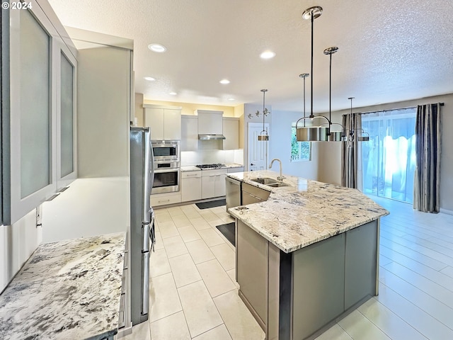 kitchen featuring sink, a textured ceiling, decorative light fixtures, a center island with sink, and appliances with stainless steel finishes