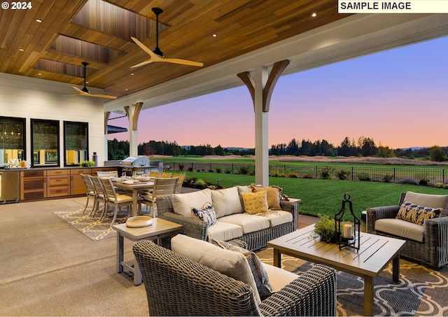 patio terrace at dusk with a rural view, a yard, an outdoor kitchen, and ceiling fan