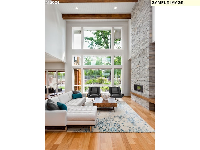 living room with a stone fireplace, a towering ceiling, a wealth of natural light, and hardwood / wood-style flooring