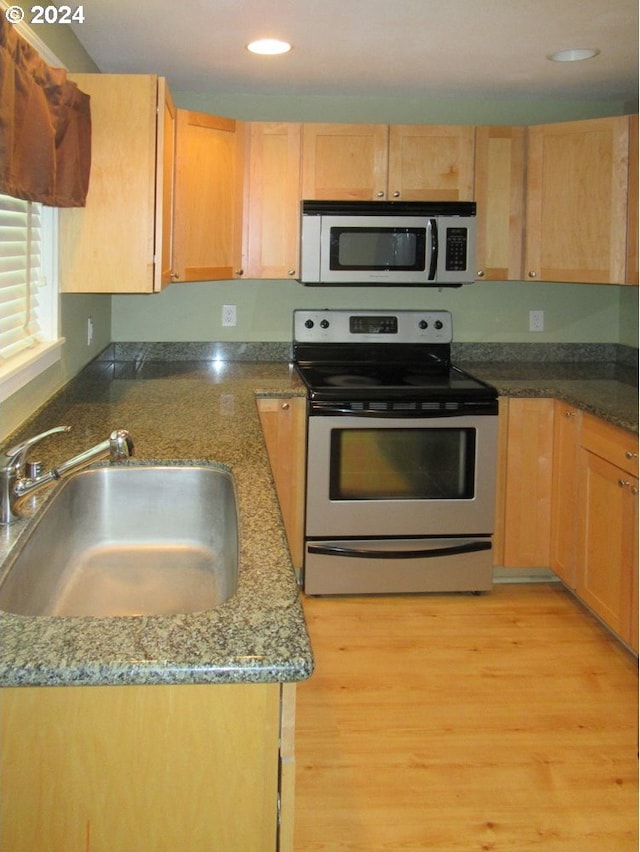 kitchen with appliances with stainless steel finishes, sink, stone counters, and light hardwood / wood-style floors