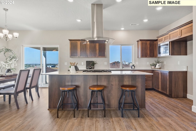 kitchen with a kitchen island, island range hood, wood finished floors, light countertops, and stainless steel microwave