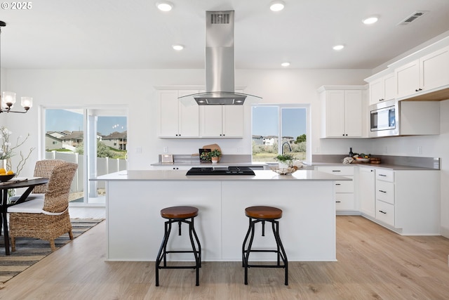 1588 NE 8th Pl, Hermiston, OR 97838 - kitchen with island exhaust hood, stainless steel microwave, a kitchen breakfast bar, a center island, and light wood finished floors