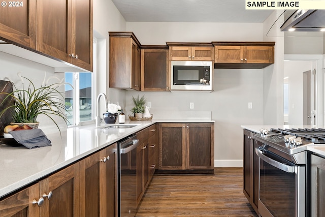 kitchen featuring baseboards, under cabinet range hood, a sink, dark wood finished floors, and stainless steel appliances