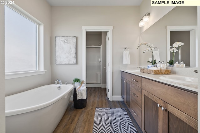 full bath featuring a sink, double vanity, a shower stall, wood finished floors, and a soaking tub