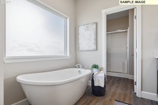 bathroom featuring wood finished floors, baseboards, a freestanding bath, and a stall shower