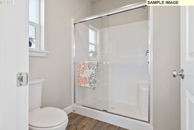 full bath featuring a stall shower, toilet, wood finished floors, and a wealth of natural light