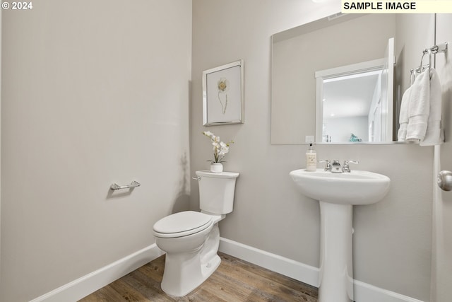 half bathroom with baseboards, wood finished floors, and toilet