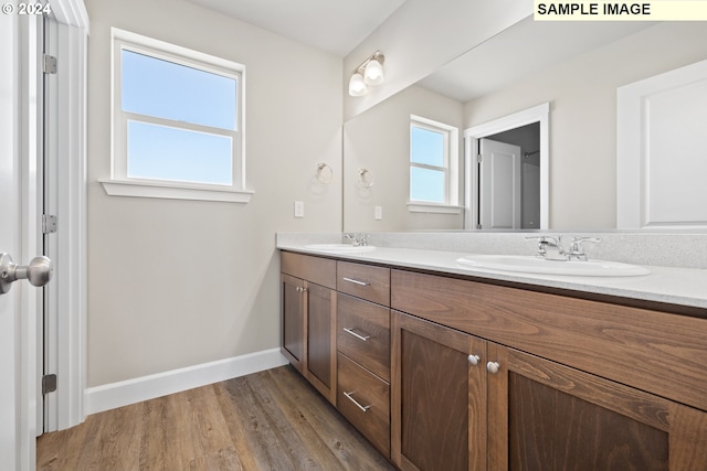 full bath featuring double vanity, a sink, baseboards, and wood finished floors
