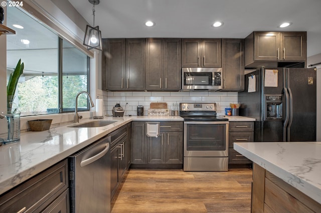 kitchen featuring sink, light hardwood / wood-style flooring, backsplash, appliances with stainless steel finishes, and decorative light fixtures