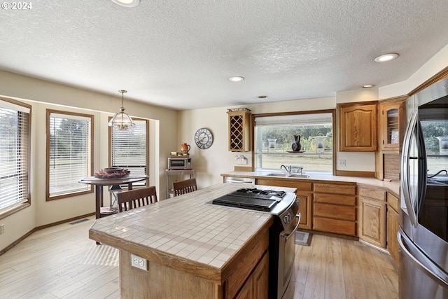 kitchen with hanging light fixtures, a healthy amount of sunlight, stainless steel appliances, and tile countertops