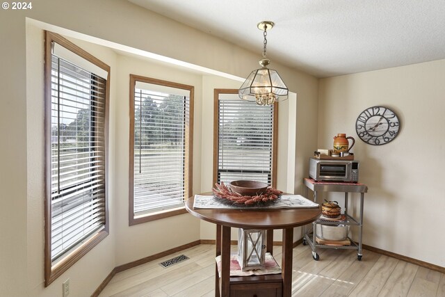 dining area with a notable chandelier, light hardwood / wood-style floors, and a textured ceiling