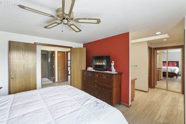 bedroom featuring ceiling fan, connected bathroom, a textured ceiling, a closet, and light hardwood / wood-style floors