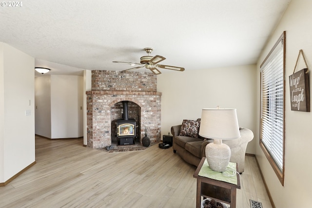 living room featuring light wood-type flooring, a textured ceiling, ceiling fan, and a wood stove