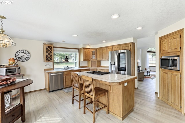 kitchen featuring hanging light fixtures, light hardwood / wood-style floors, a kitchen island, stainless steel appliances, and a notable chandelier