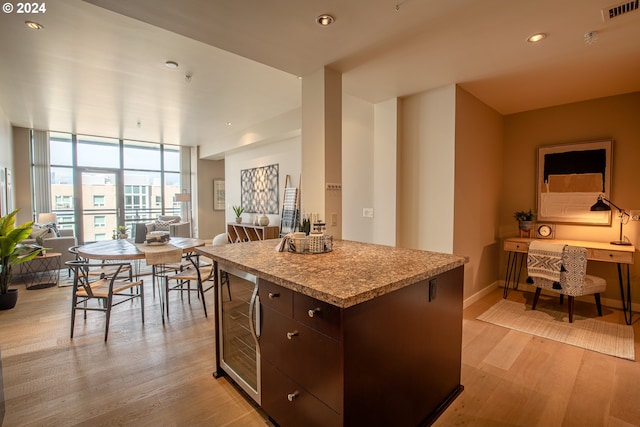 kitchen featuring a center island, light hardwood / wood-style flooring, dark brown cabinets, a wall of windows, and beverage cooler